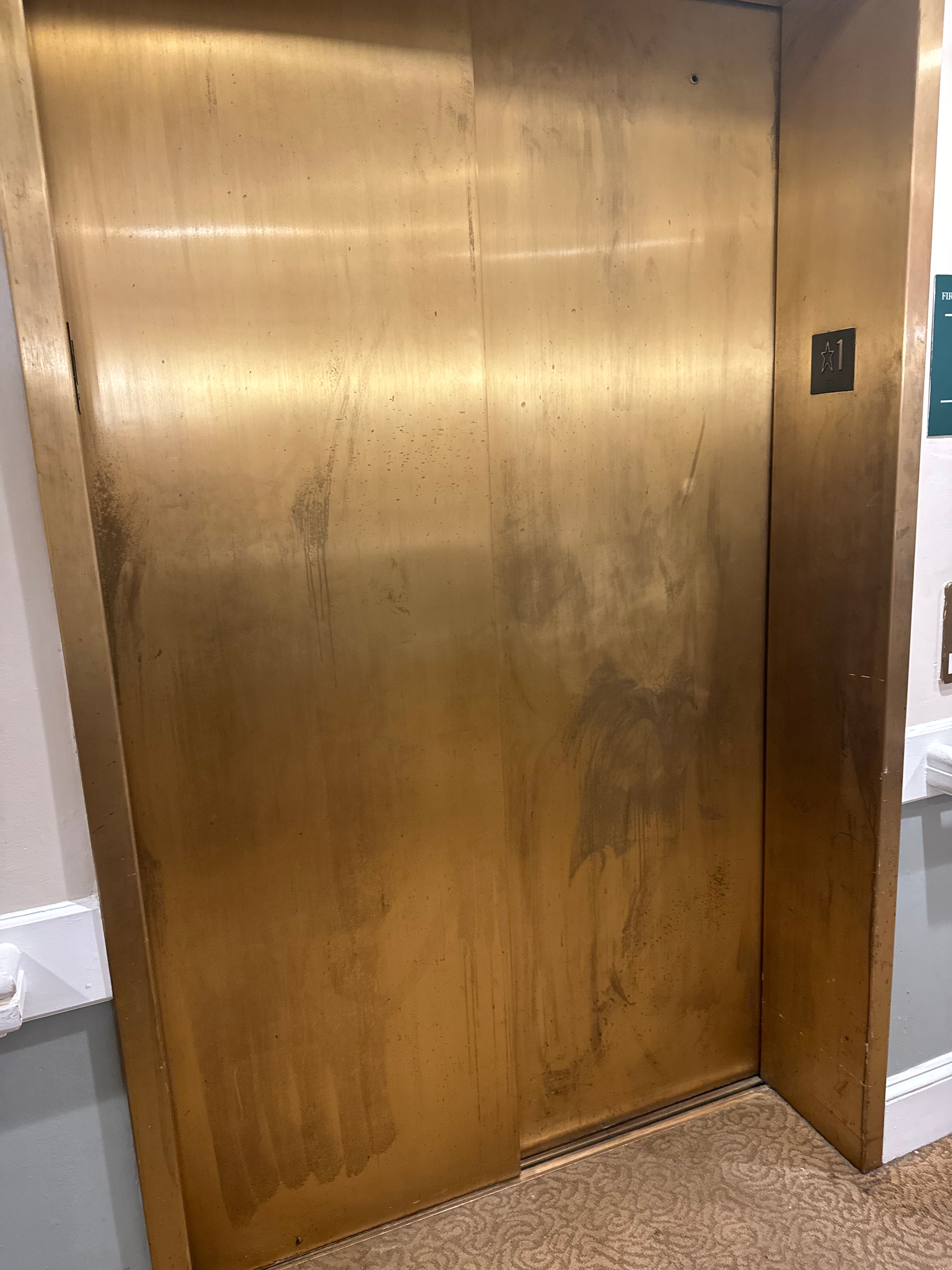 Brass elevator door panel before restoration — tarnished and worn
