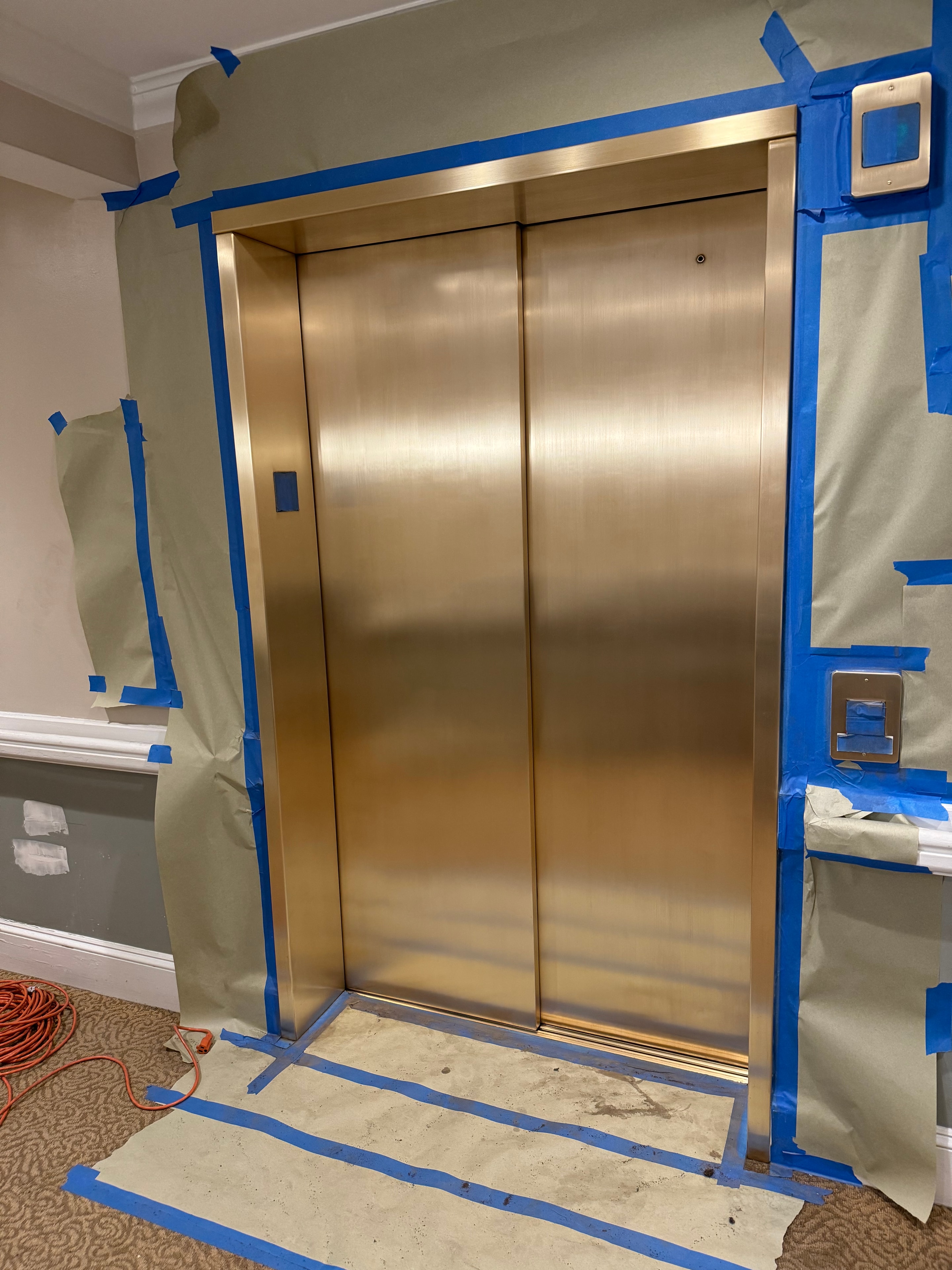 Stainless steel elevator cab restoration in progress — blue tape masking
